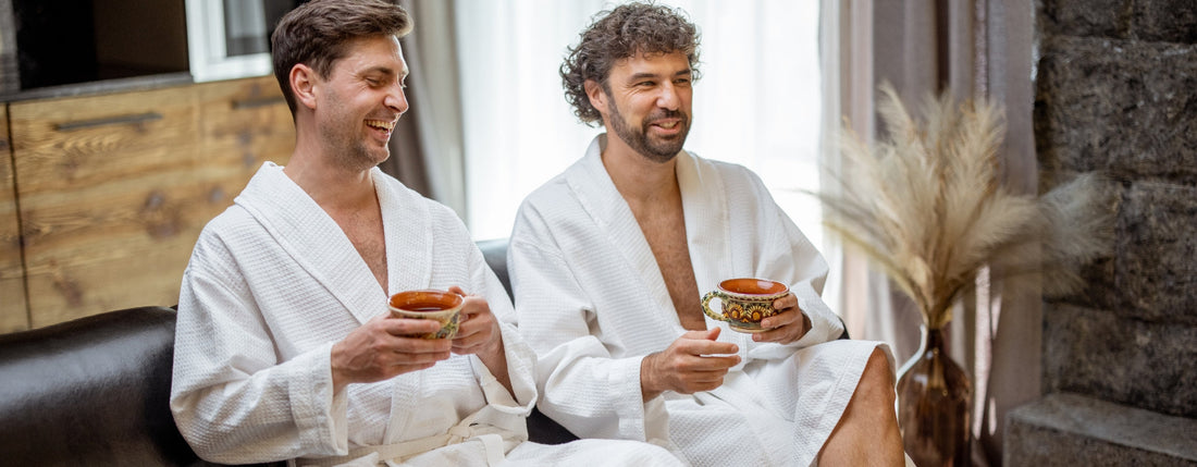 Deux hommes en peignoir de bain blanc assis sur un canapé, une tasse à la main